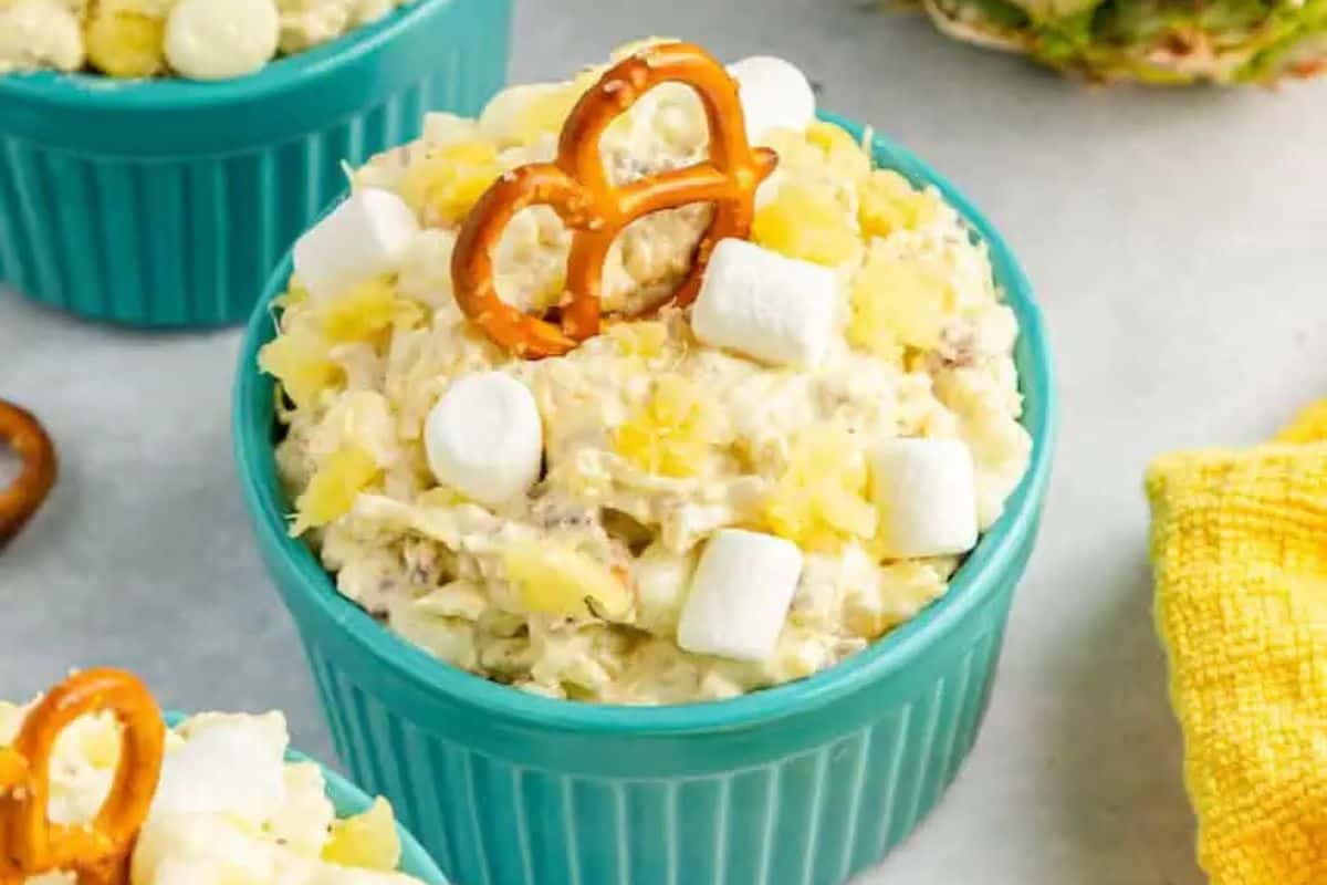 A blue bowl filled with a creamy salad of marshmallows and pineapple chunks, topped with a pretzel—one of the prettiest desserts perfect for spring recipes.