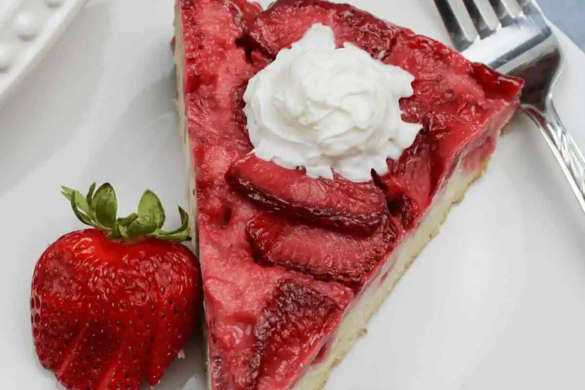 A slice of strawberry-topped pie with whipped cream, served on a white plate with a fresh strawberry and a fork—one of the prettiest desserts and perfect for spring recipes.