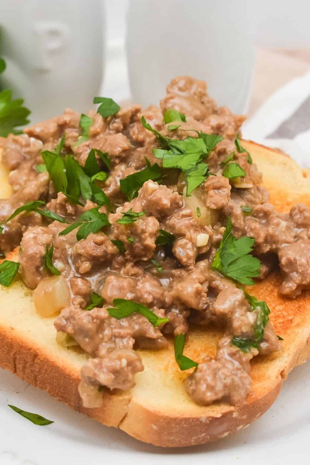 A slice of toasted bread topped with ground beef in a creamy hamburger gravy sauce, garnished with chopped parsley.