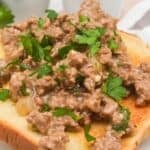 A slice of toasted bread topped with ground beef in a creamy hamburger gravy sauce, garnished with chopped parsley.