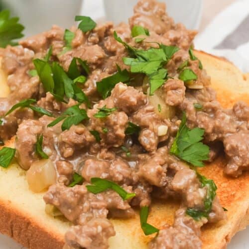 A slice of toasted bread topped with ground beef in a creamy hamburger gravy sauce, garnished with chopped parsley.