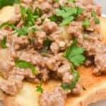 A slice of toasted bread topped with creamy hamburger gravy and chopped fresh parsley on a white plate.