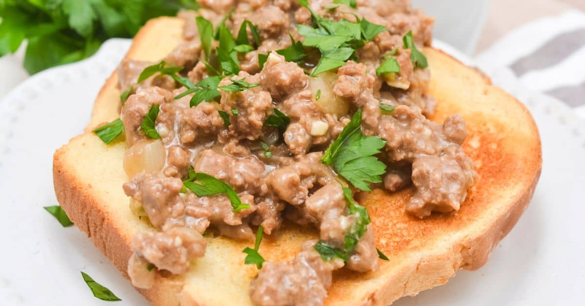 A slice of toasted bread topped with creamy hamburger gravy and chopped fresh parsley on a white plate.