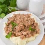 A plate of mashed potatoes topped with garnished with parsley, sits next to salt and pepper shakers and fresh parsley.