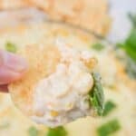 A hand holding a chip with the cream cheese corn dip.