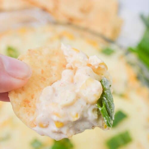 A hand holding a chip with the cream cheese corn dip.