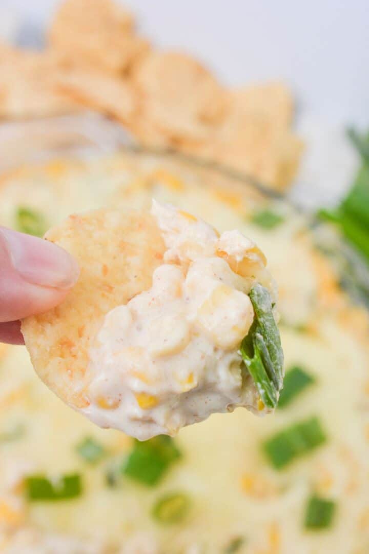 A hand holding a chip with the cream cheese corn dip.