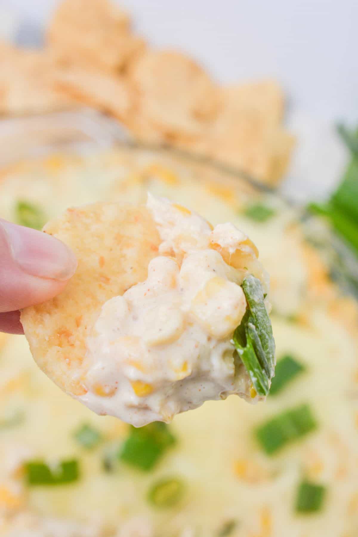 A hand holding a chip with the cream cheese corn dip.