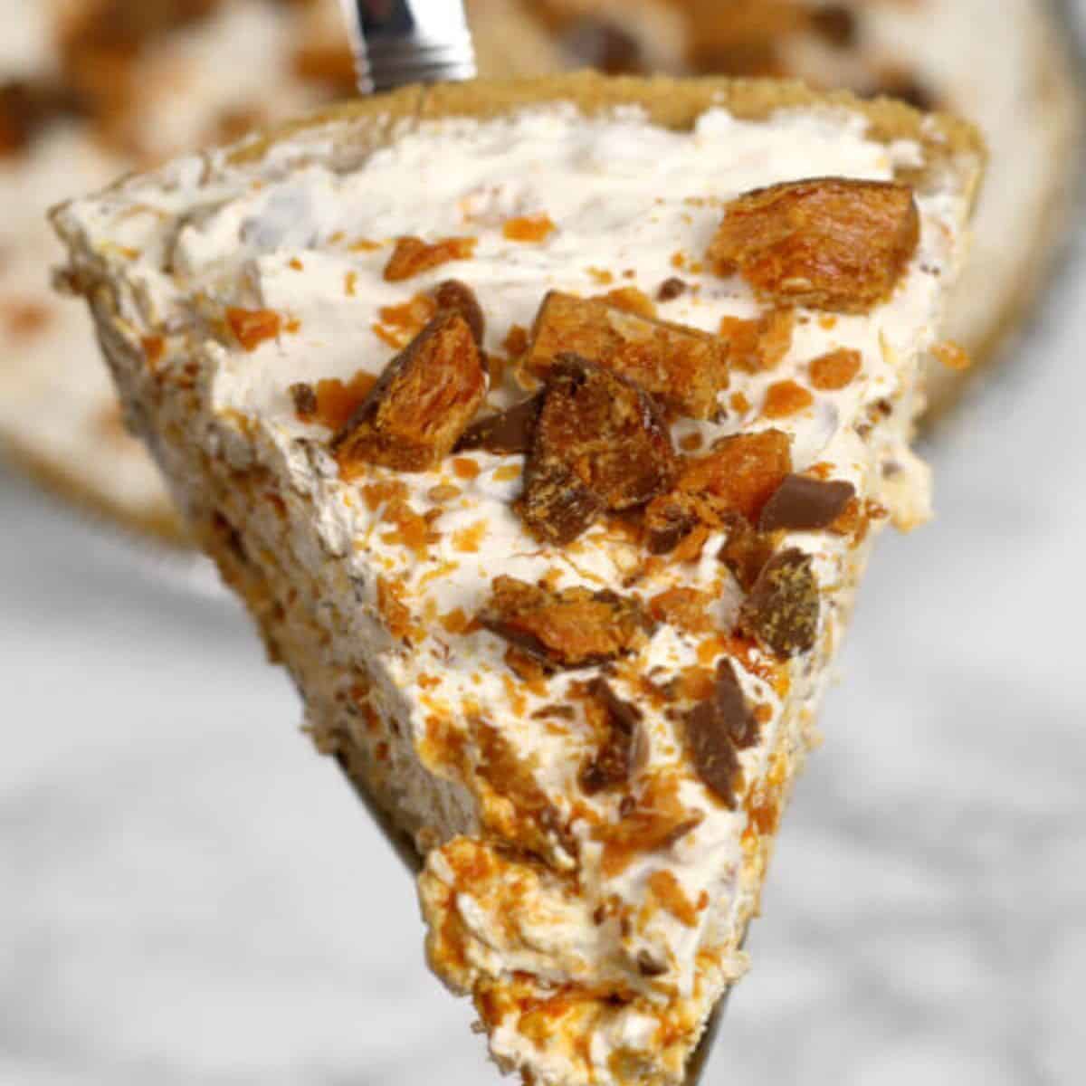 A close-up of a pie slice with a creamy filling, topped with crushed toffee or candy pieces, being lifted from the pie—this dessert is truly an It's a Keeper treat.