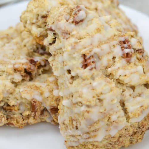 A close-up of cinnamon scones and glazed pecan scones stacked on a white plate.