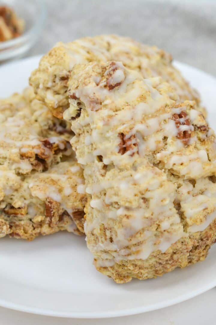 A close-up of cinnamon scones and glazed pecan scones stacked on a white plate.