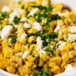 A bowl of corn salad garnished with cheese and chopped herbs, perfect for your collection of summer side dishes, with text overlay reading "15 Go-To Summer Side Dishes.