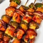Grilled Chicken Kabobs with pieces of glazed chicken, green bell pepper, pineapple, and red onion are arranged on a white plate.