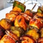 Grilled BBQ Chicken skewers with chunks of chicken, green bell pepper, red onion, and pineapple arranged on a white plate.