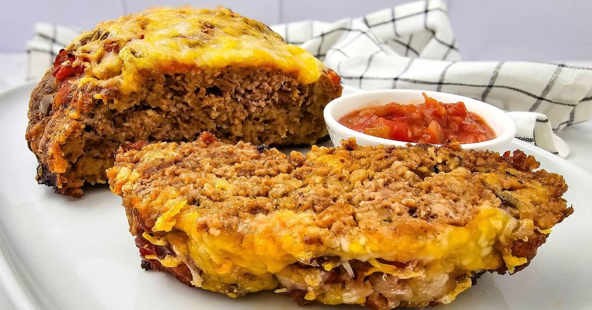 Two slices of salsa meatloaf topped with melted cheese, served with a small bowl of salsa.