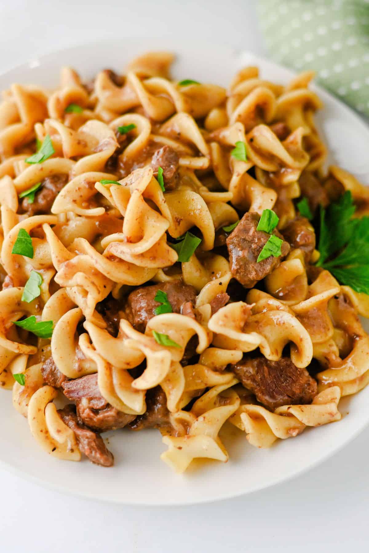 A white plate of beef and noodles in a creamy stroganoff sauce, garnished with parsley.