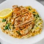 Sliced lemon chicken served over orzo pasta with spinach, topped with a fresh lemon wedge.