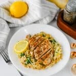 Sliced meat served over pasta with spinach on a white plate with a fork.