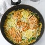 Sliced breasts with spinach and shredded cheese served over pasta in a skillet.