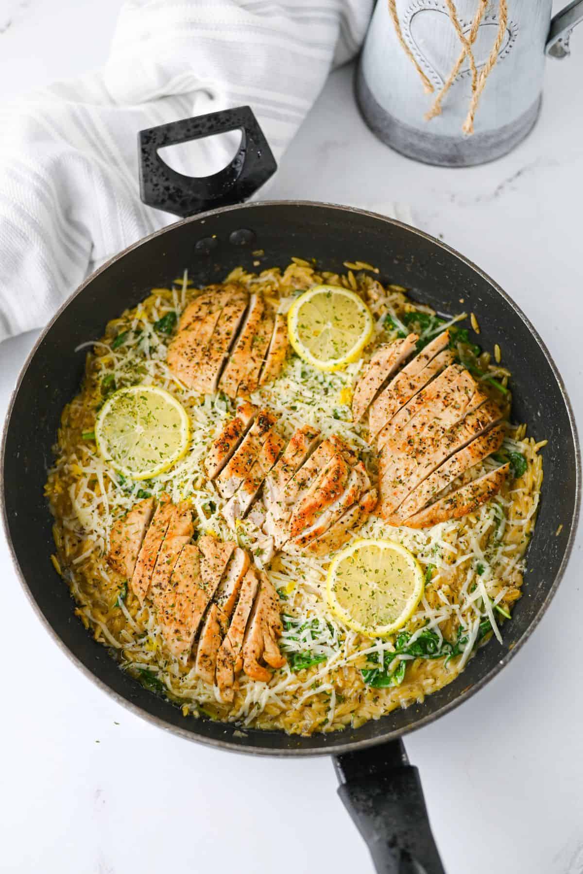 Sliced breasts with spinach and shredded cheese served over pasta in a skillet.