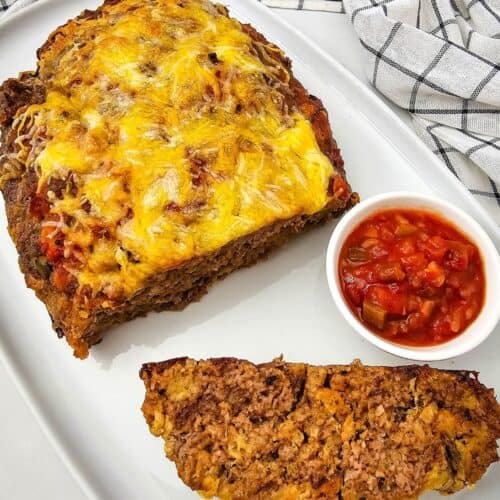 A sliced salsa meatloaf topped with melted cheese on a platter next to a small bowl of salsa.