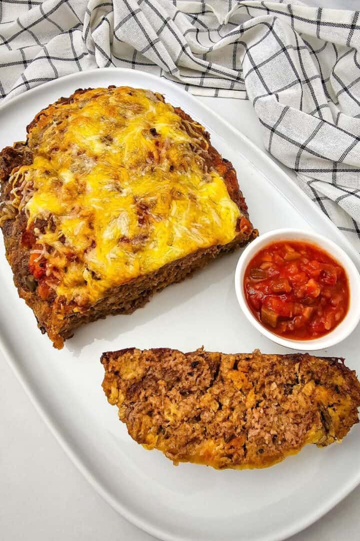 A sliced salsa meatloaf topped with melted cheese on a platter next to a small bowl of salsa.